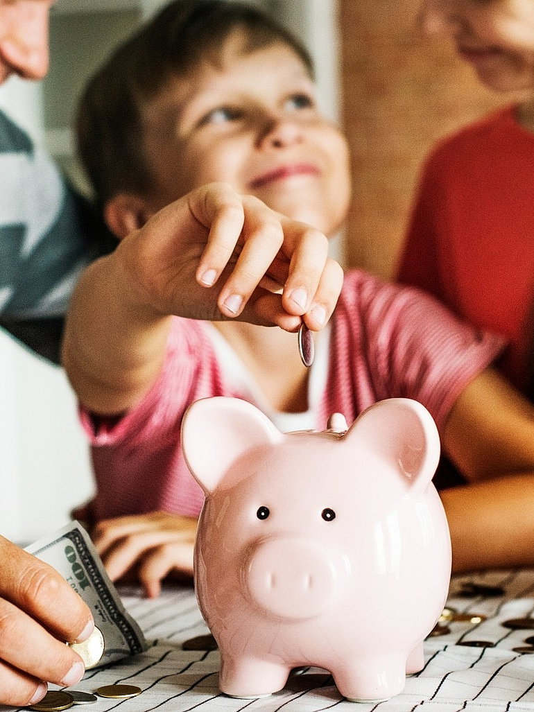 Kind mit Eltern sitzt am Tisch und wirft Geld in sein Sparschwein