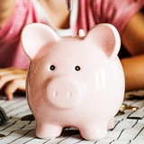 Kind mit Eltern sitzt am Tisch und wirft Geld in sein Sparschwein