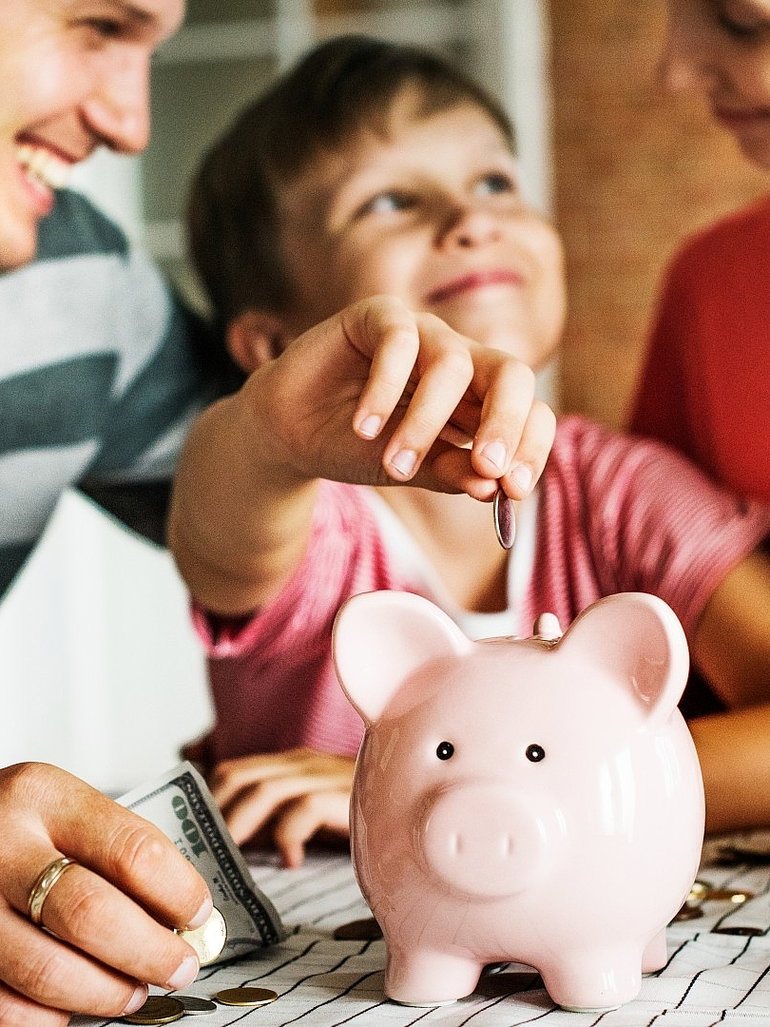 Kind packt geld in sein sparschwein mit seinen eltern