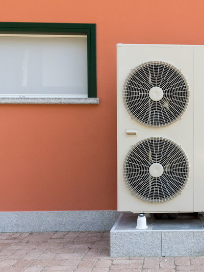 Bild von einer Wärmepumpe vor einer orangenen Hauswand